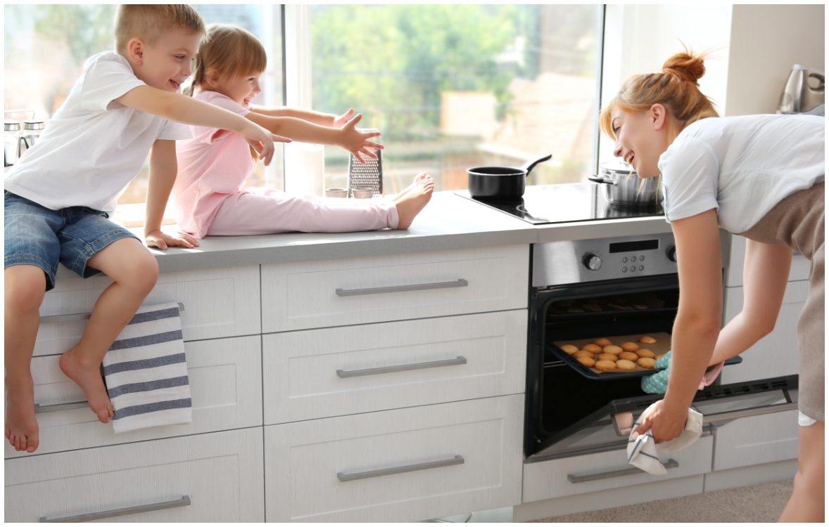 mother opening oven with kids on countertop