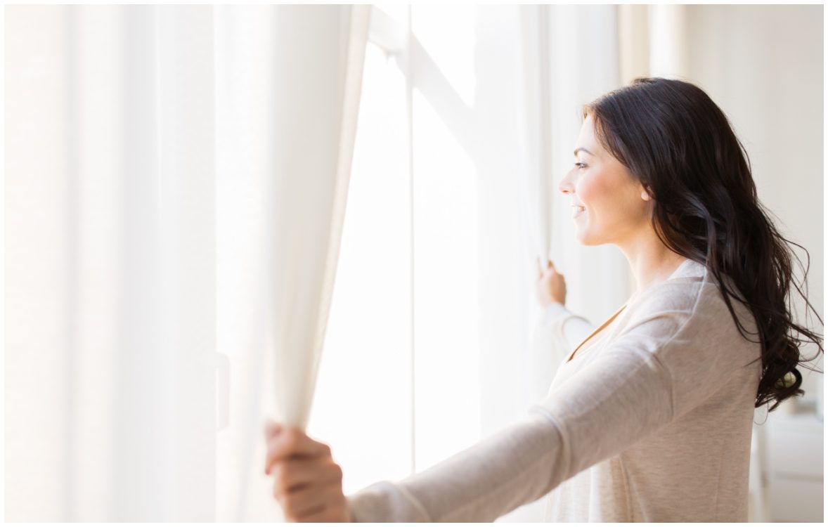 women pulling back window curtains